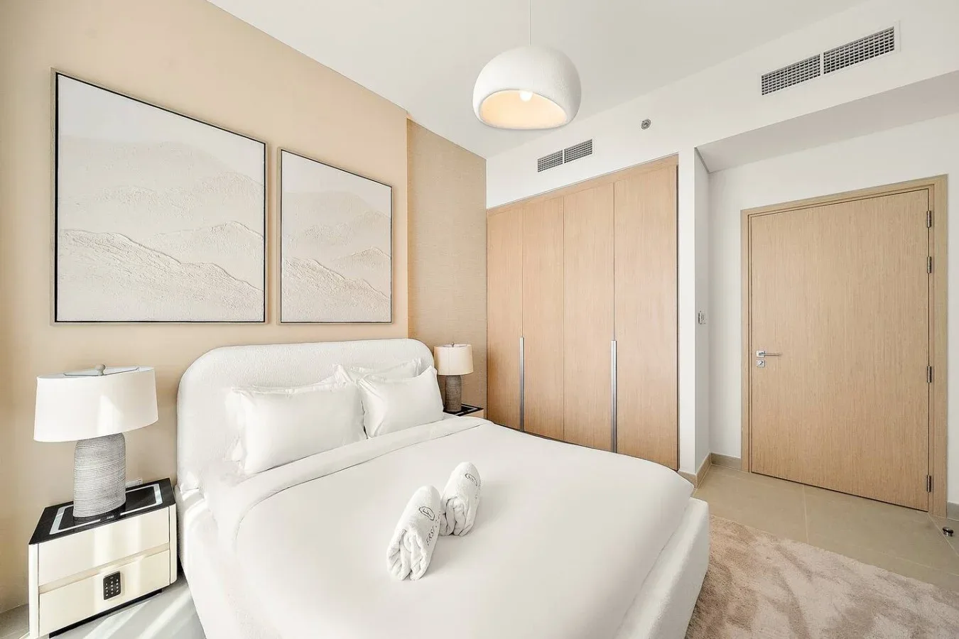 A bright bedroom with a neatly made bed and light wood wardrobes.