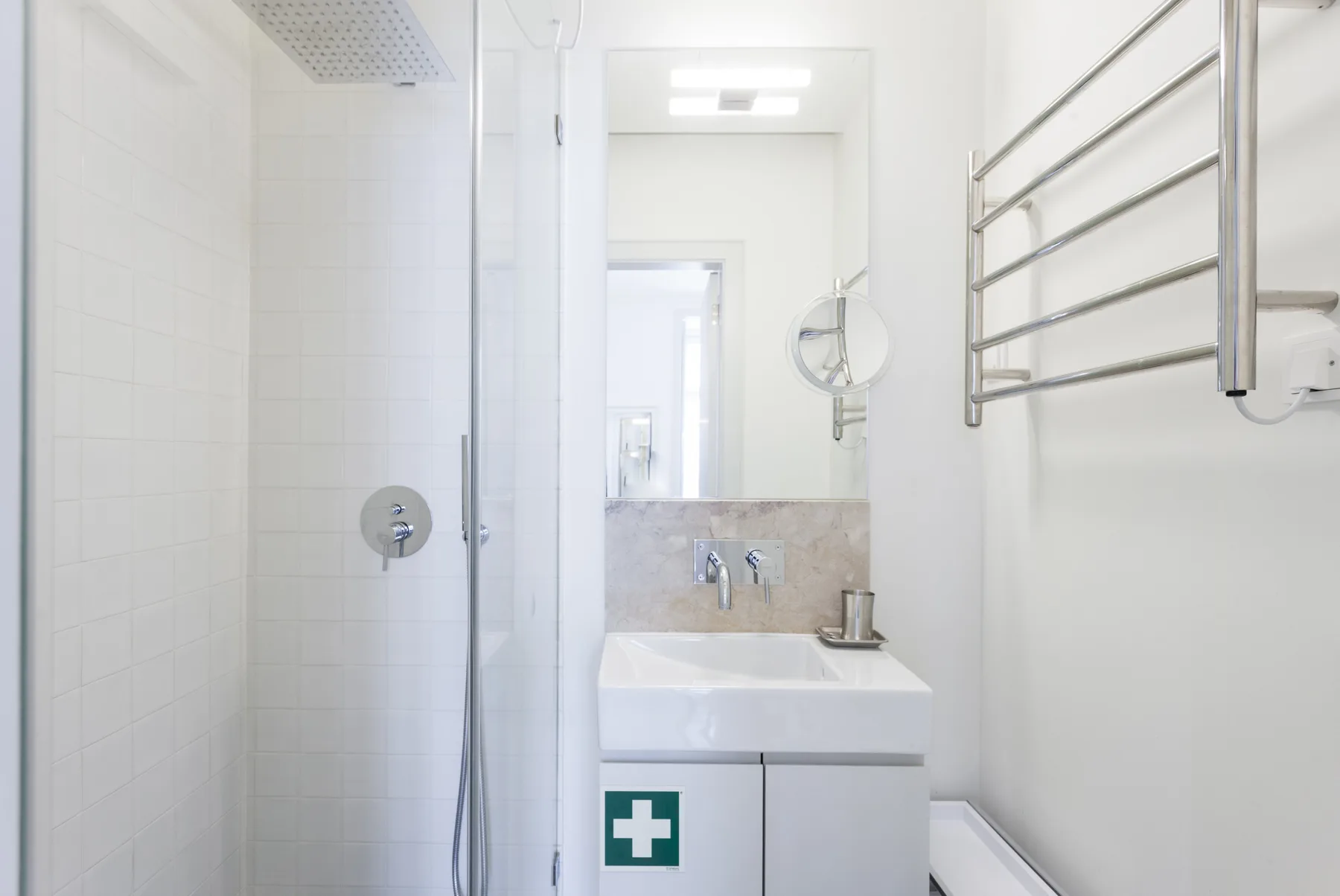 Un baño luminoso con ducha, lavabo y toallero de pared.