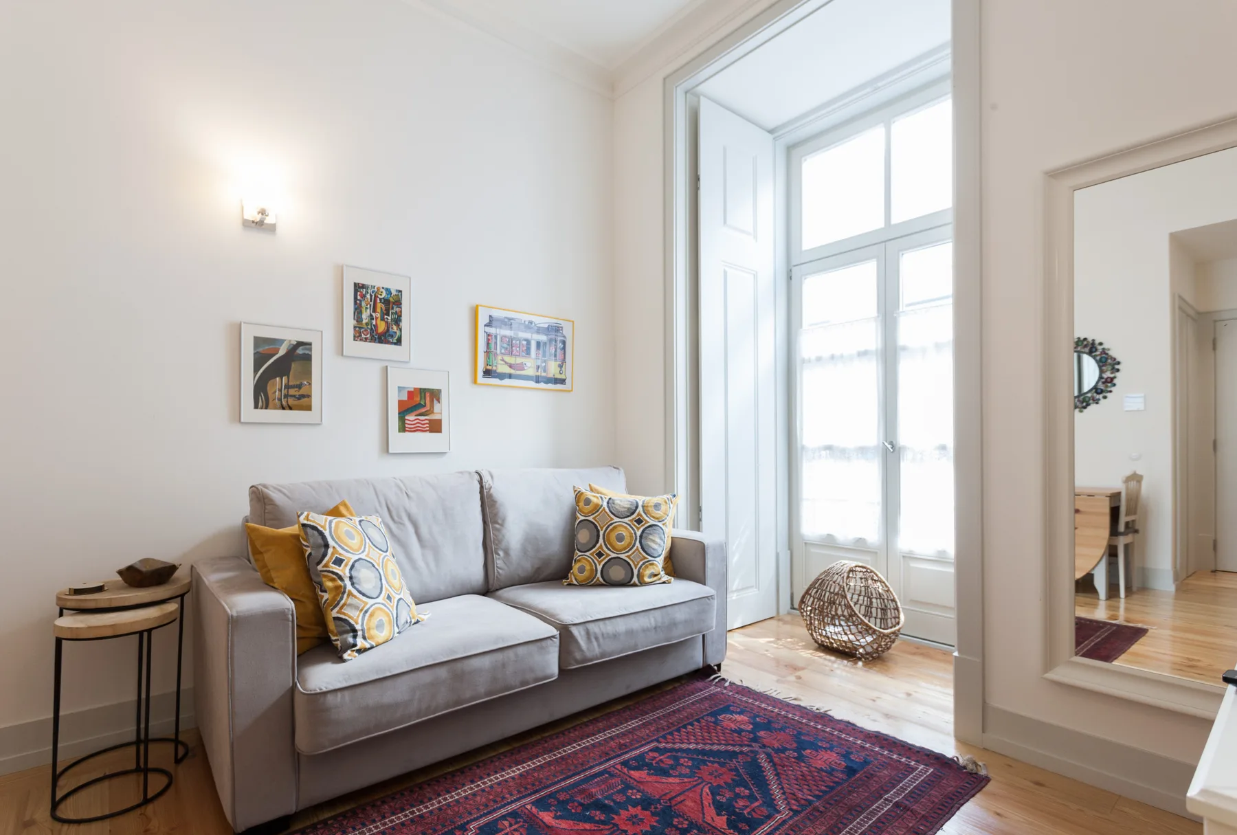 Una sala de estar con un sofá gris, cojines coloridos y una ventana grande.