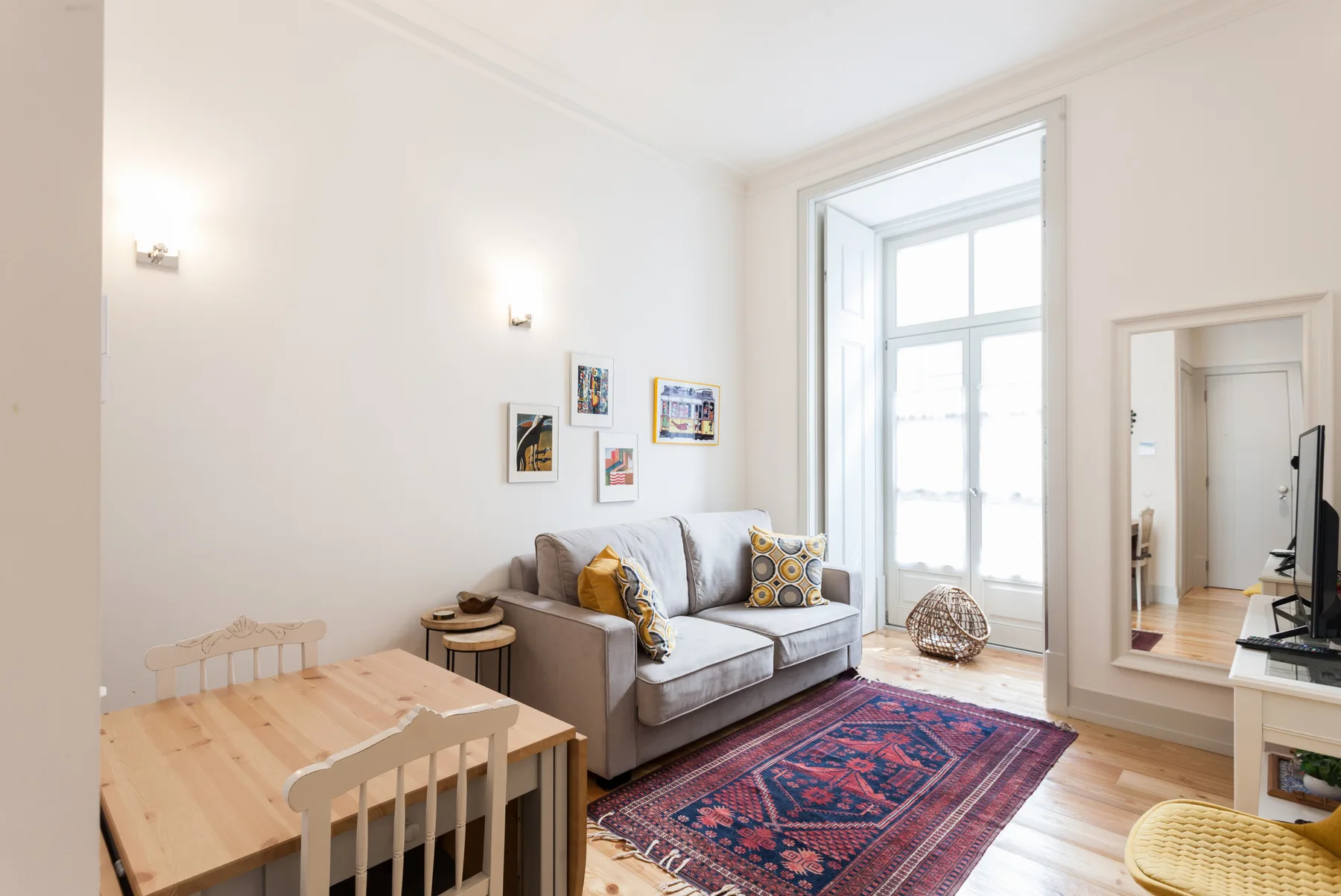 Una sala luminosa con asientos, una mesa de comedor de madera y una alfombra estampada.