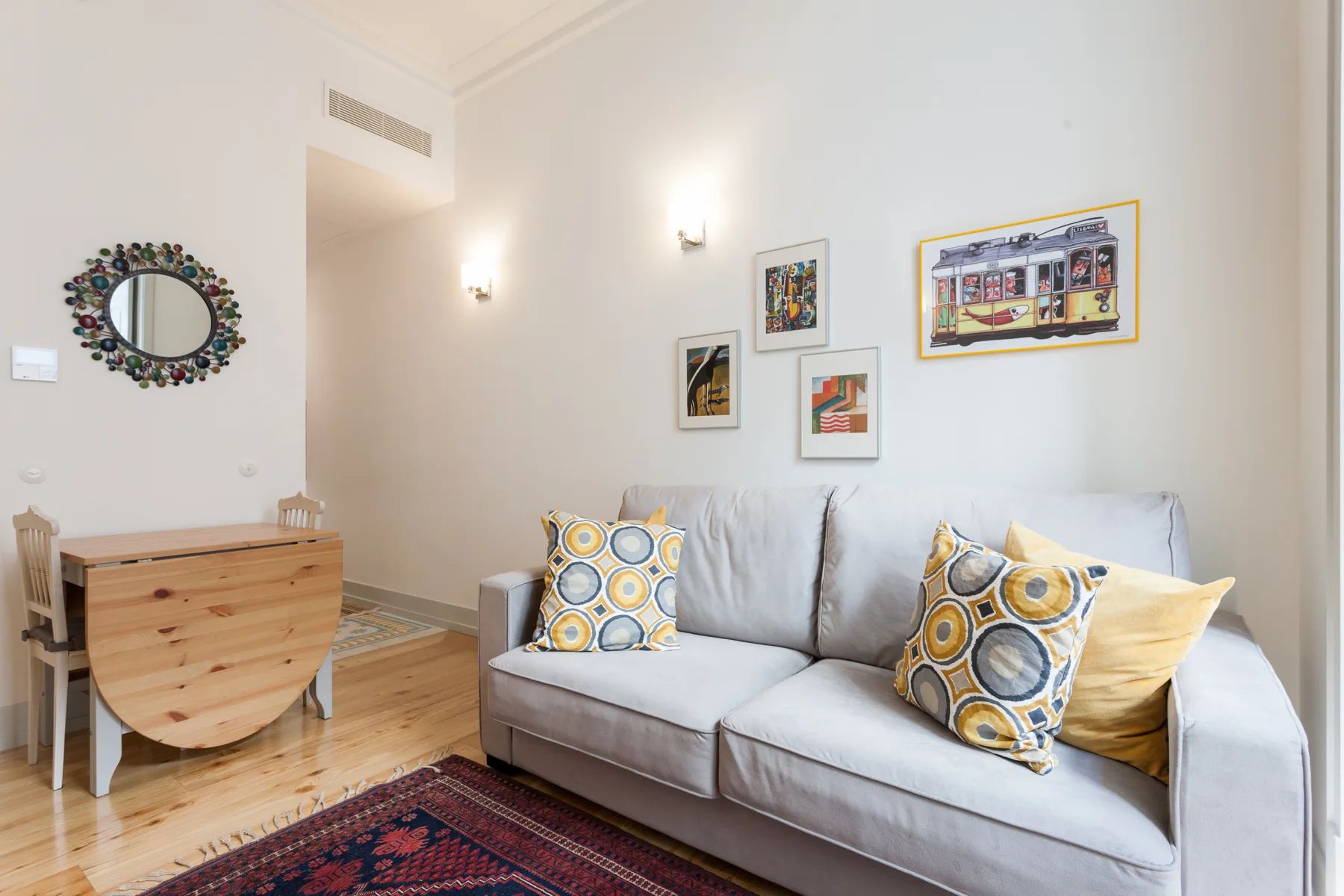 Sala de estar con sofá gris, cojines estampados y cuadros enmarcados.