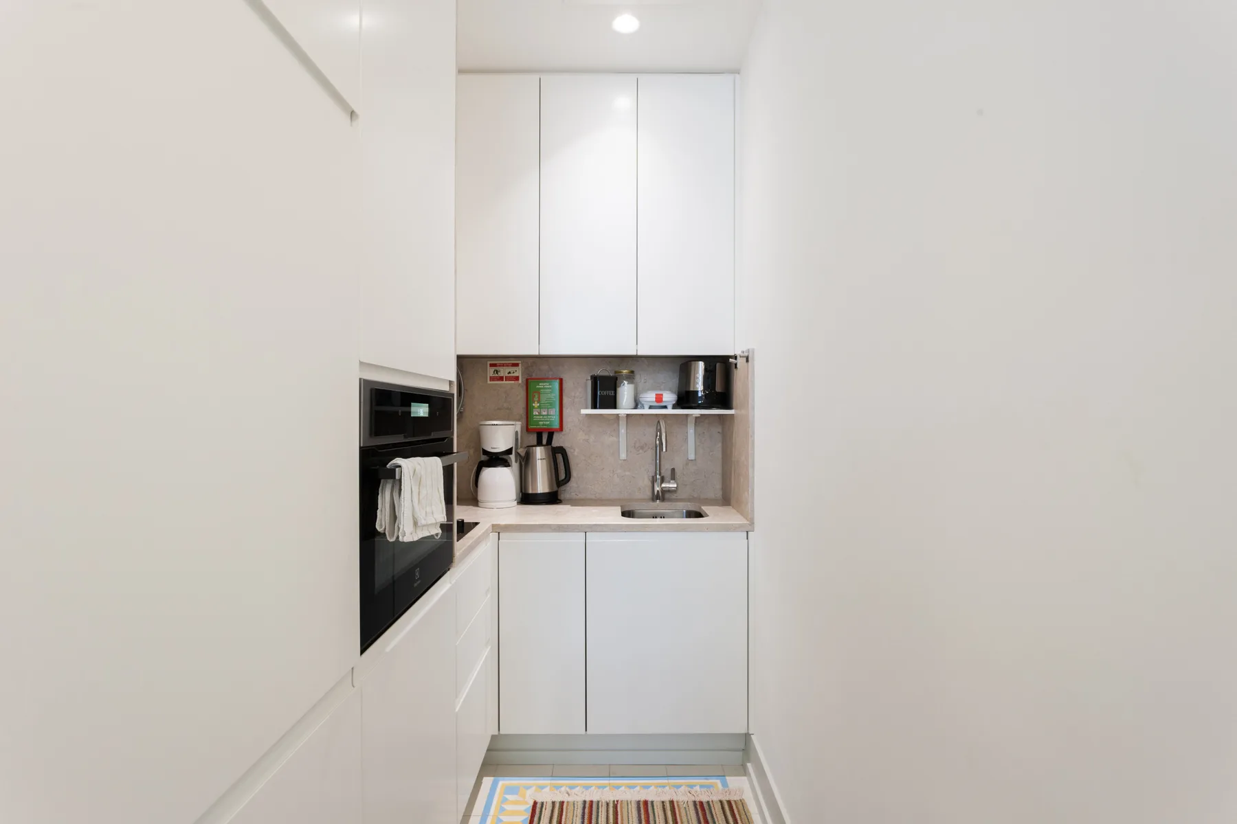 Una cocina compacta con armarios blancos, encimera y electrodomésticos integrados.