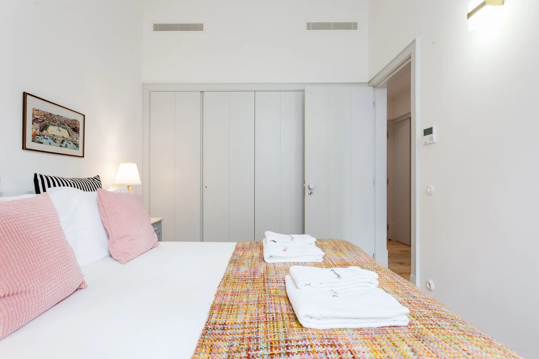 Un dormitorio luminoso con una cama tendida y toallas dobladas.