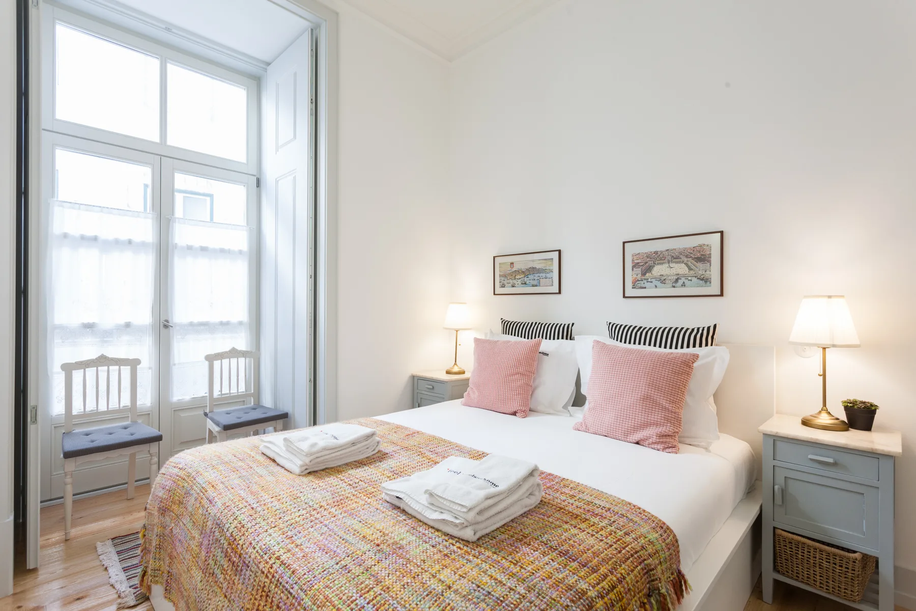 Dormitorio luminoso con cama doble, colcha estampada y ventanas altas.