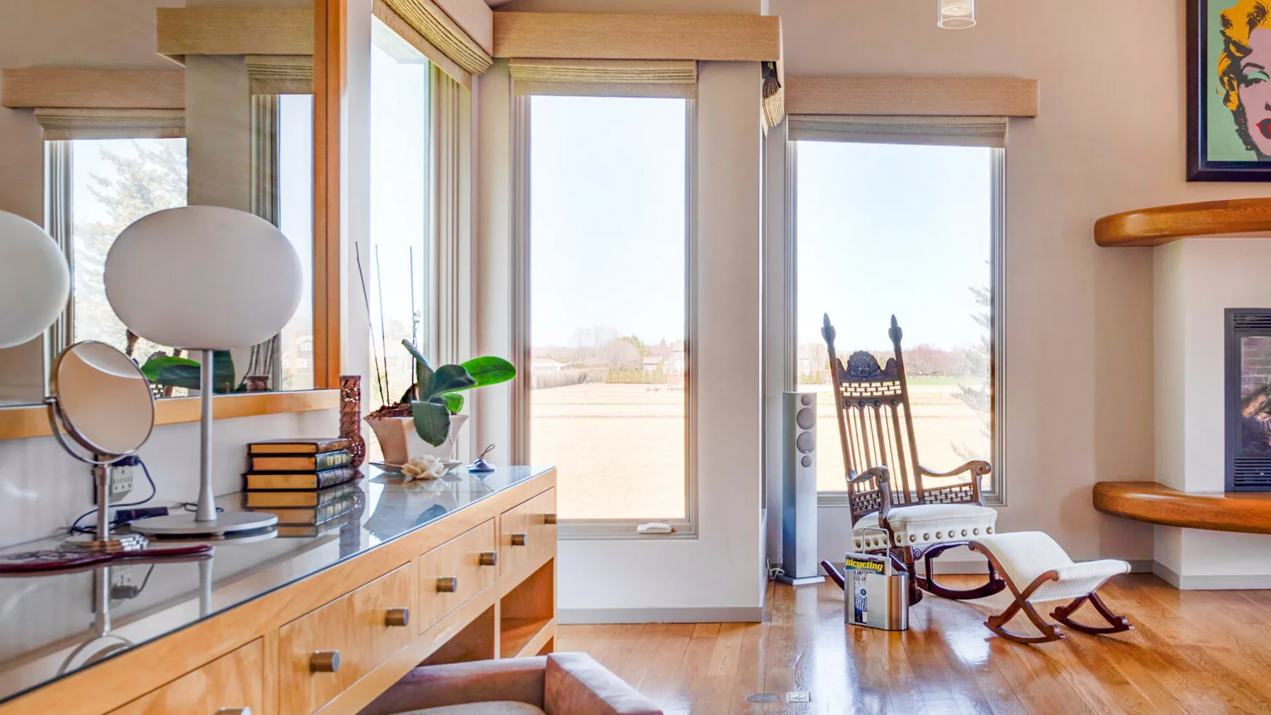 Una sala luminosa con ventanales, una mecedora y un mueble bajo de madera.