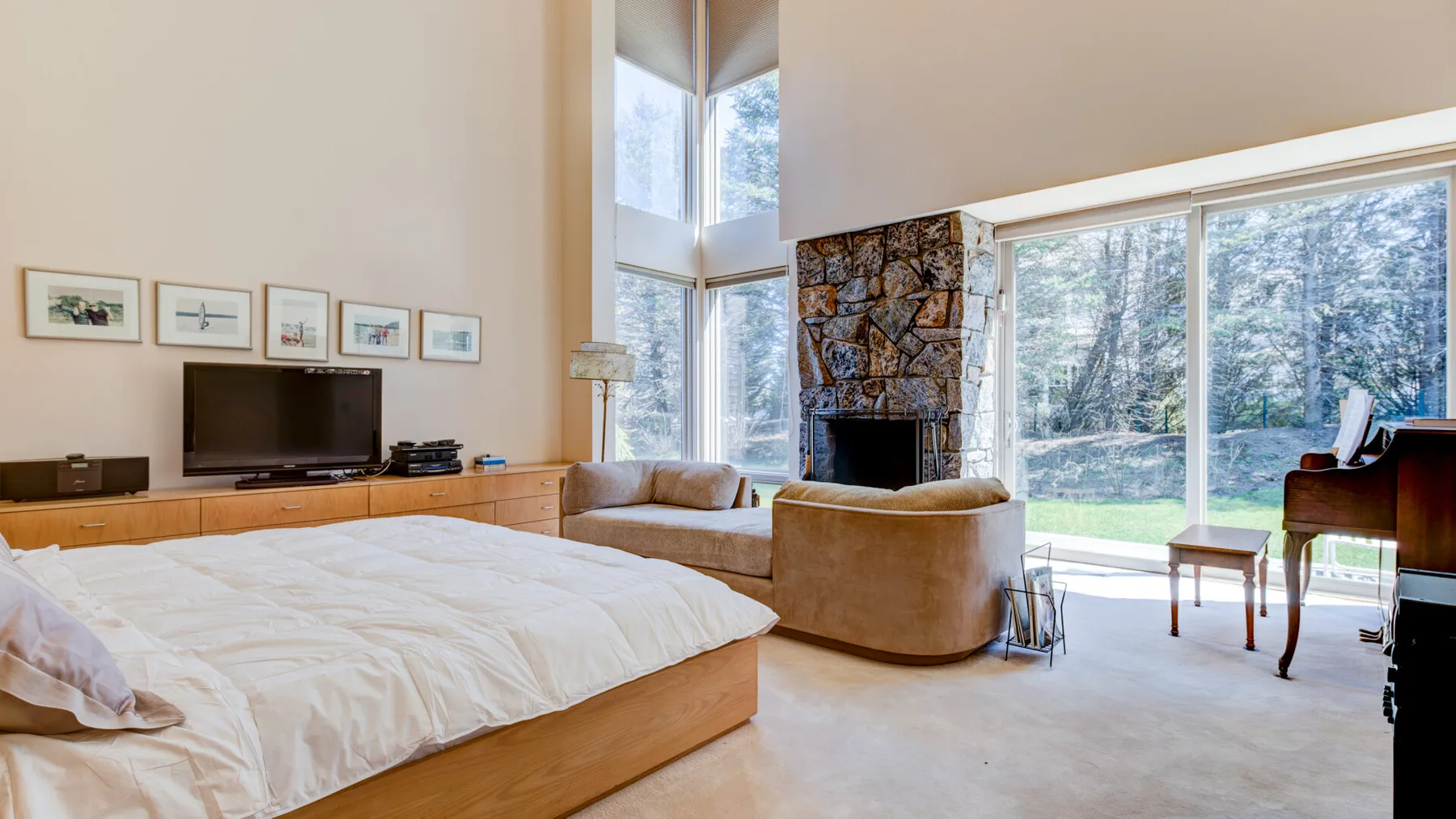 Un dormitorio con una cama y asientos junto a grandes ventanas y una chimenea de piedra.