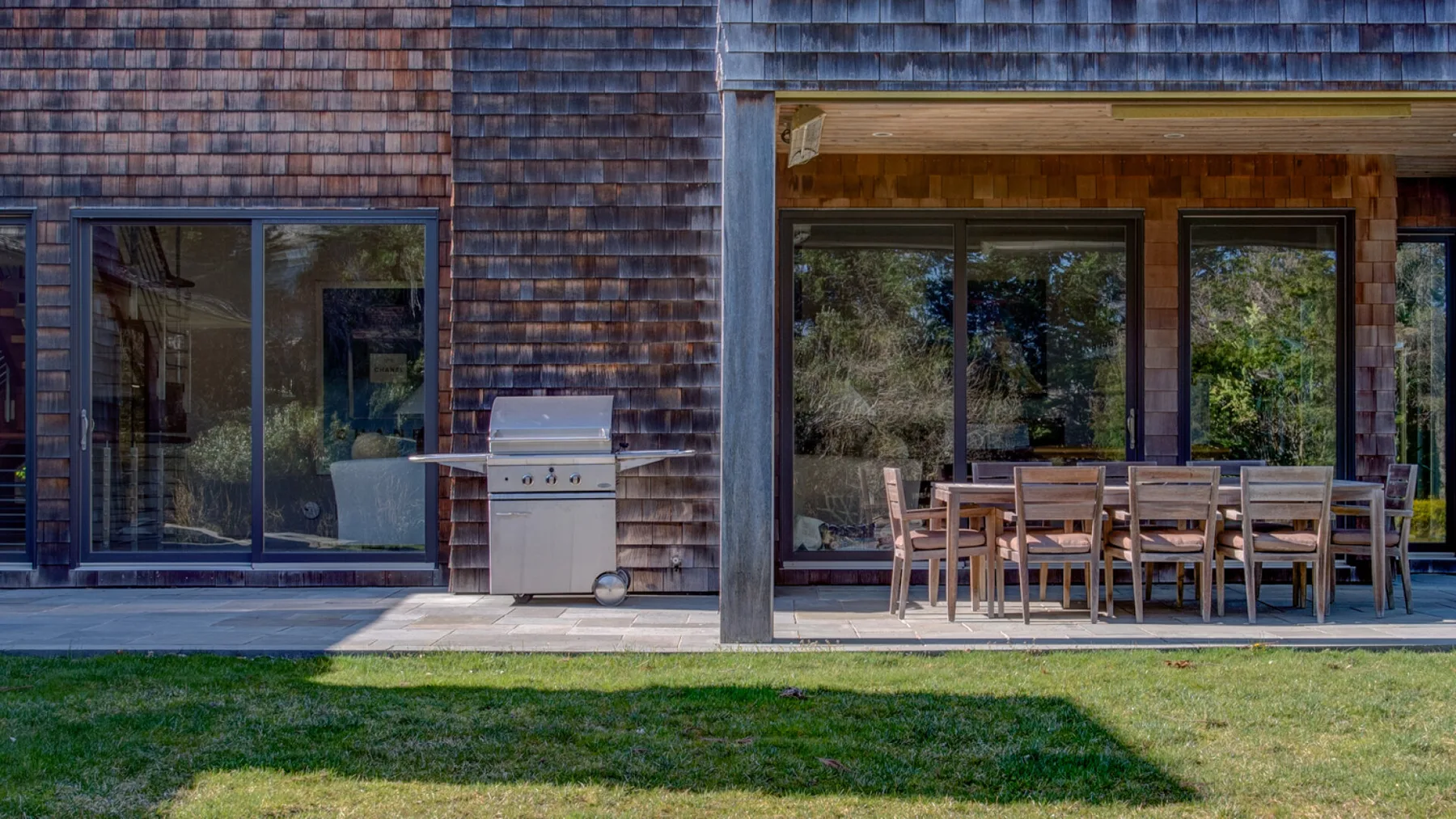 Una zona cubierta para comer al aire libre, con mesa y asientos junto a la casa.