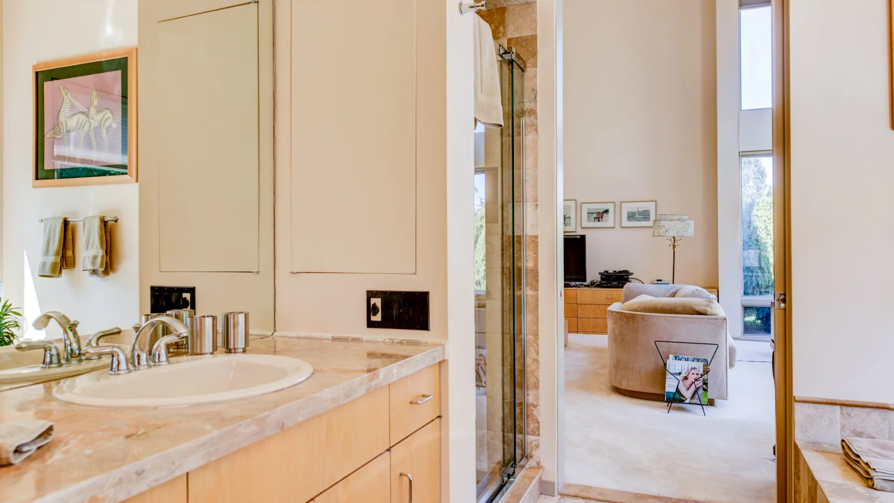 Un lavabo de baño da a una sala de estar con asientos y ventanas altas.
