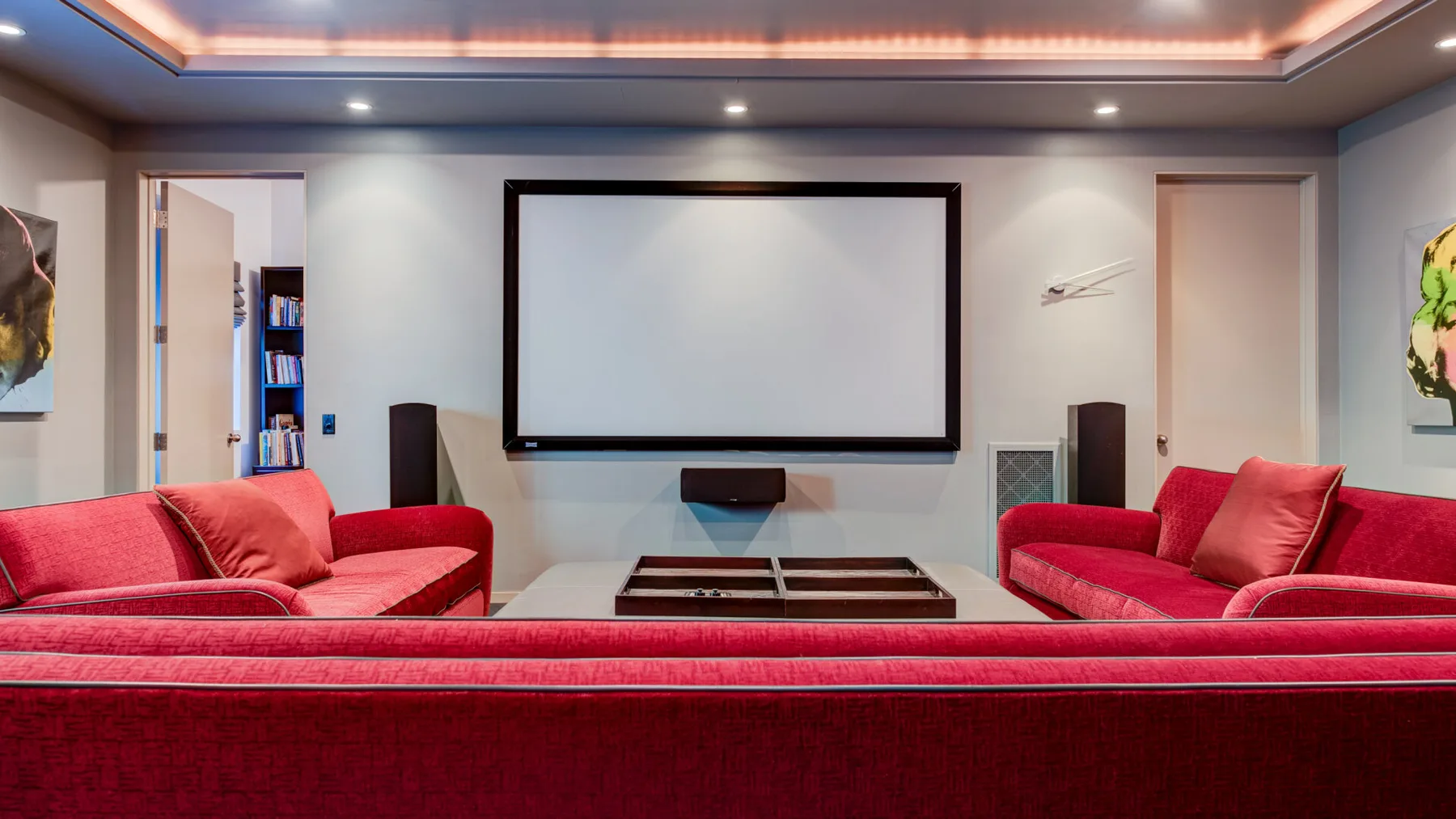 Un cine en casa con asientos rojos frente a una gran pantalla de proyección.