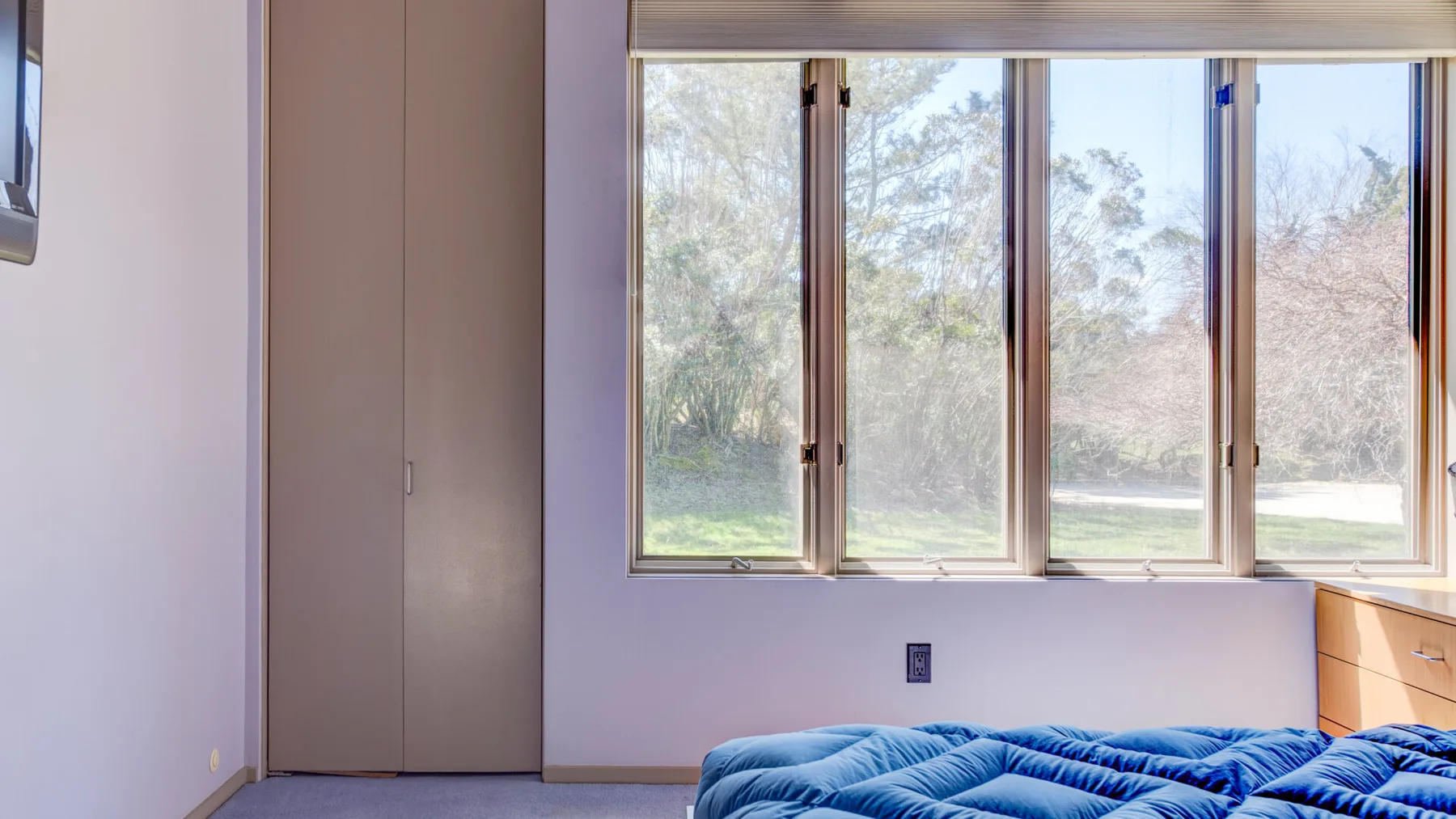 Un dormitorio con una cama bajo una amplia ventana con vista a los árboles.