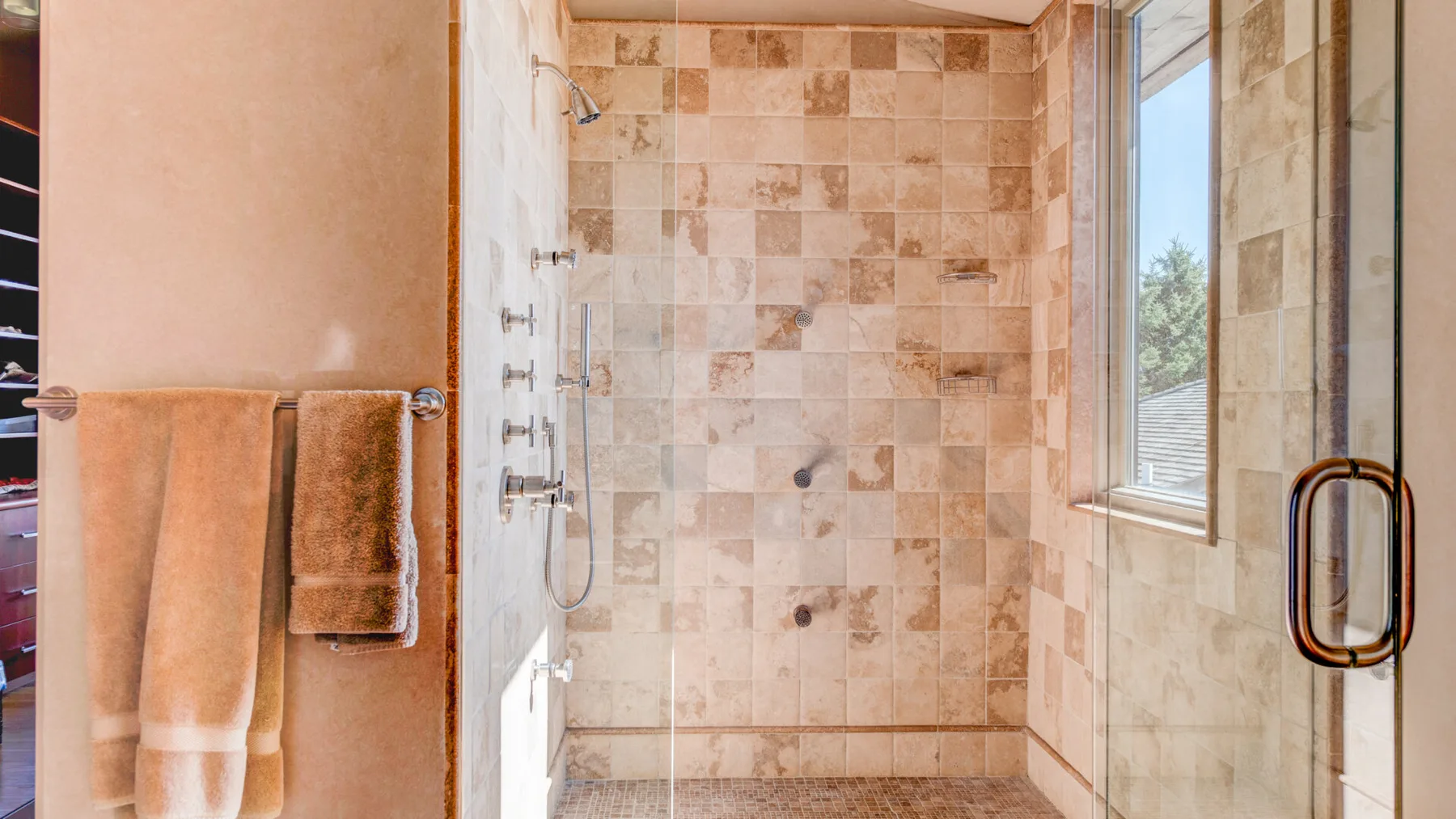 Zona de ducha de baño con azulejos, una ventana y toallas colgadas.