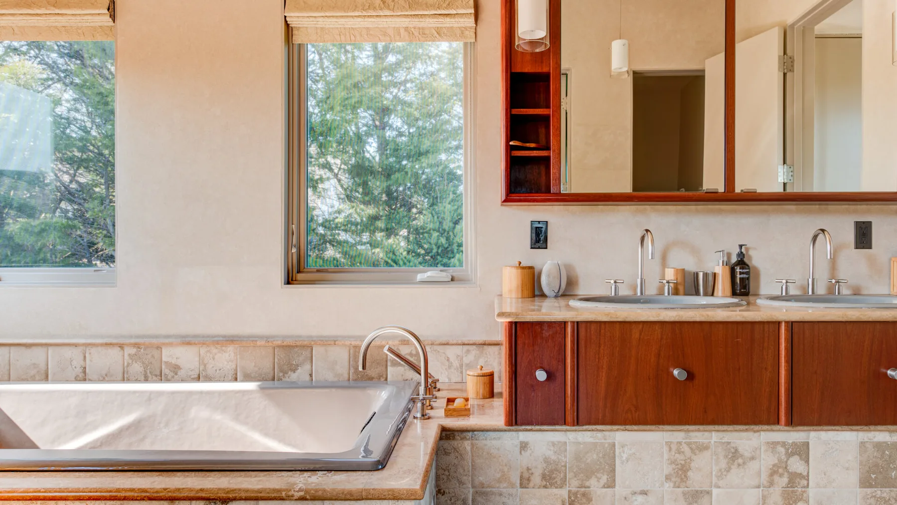 Un mueble de baño con lavabo está junto a una bañera empotrada bajo ventanas grandes.