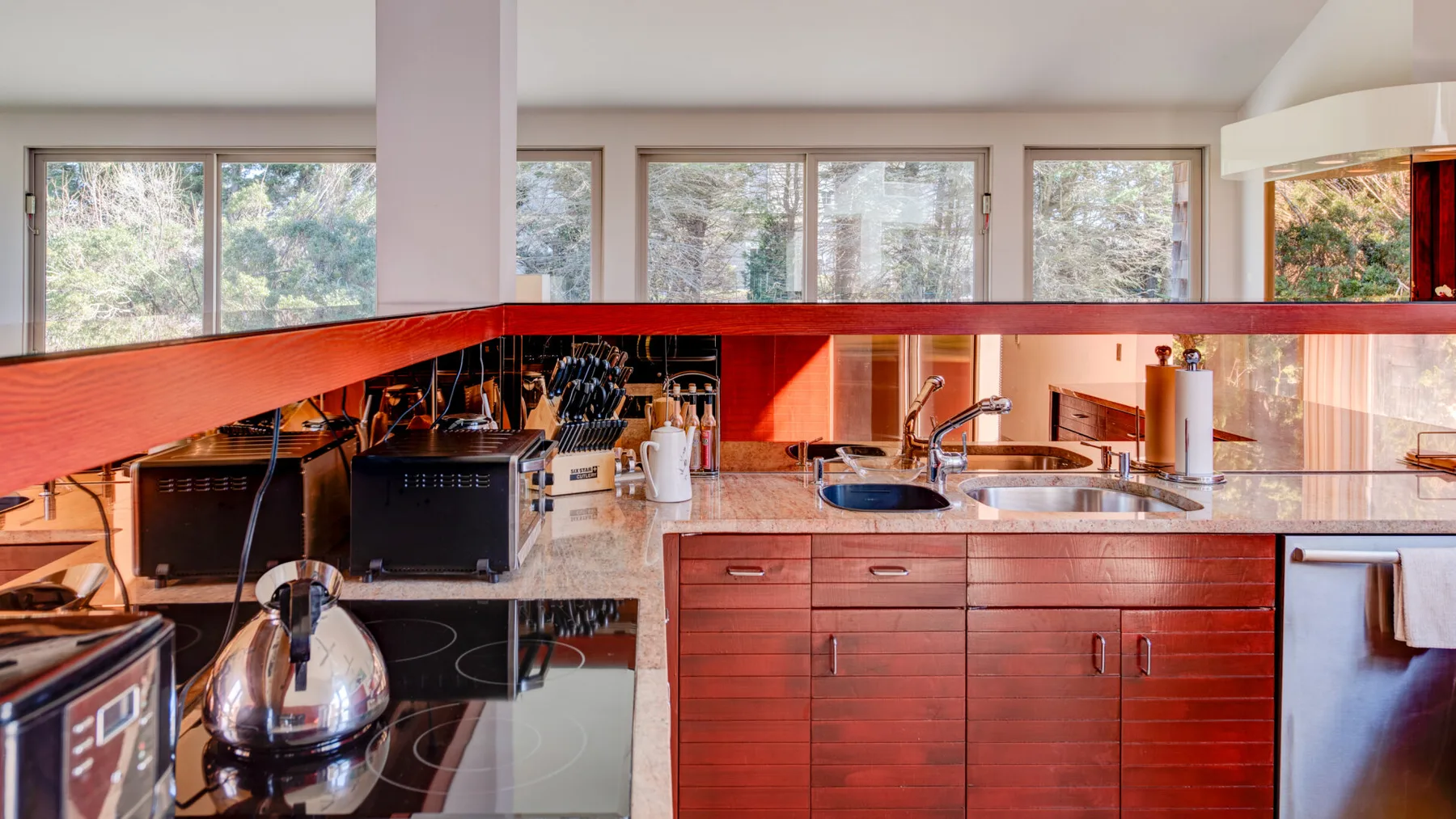 Una cocina con gabinetes de madera, un fregadero y ventanas grandes.