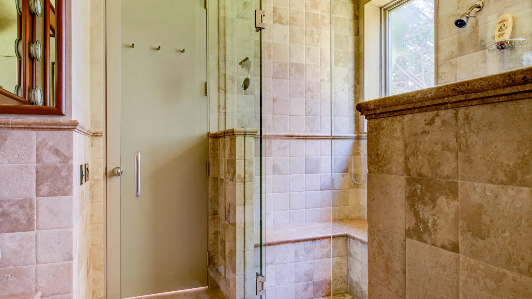 Un baño con azulejos, una ducha de vidrio y una ventana.