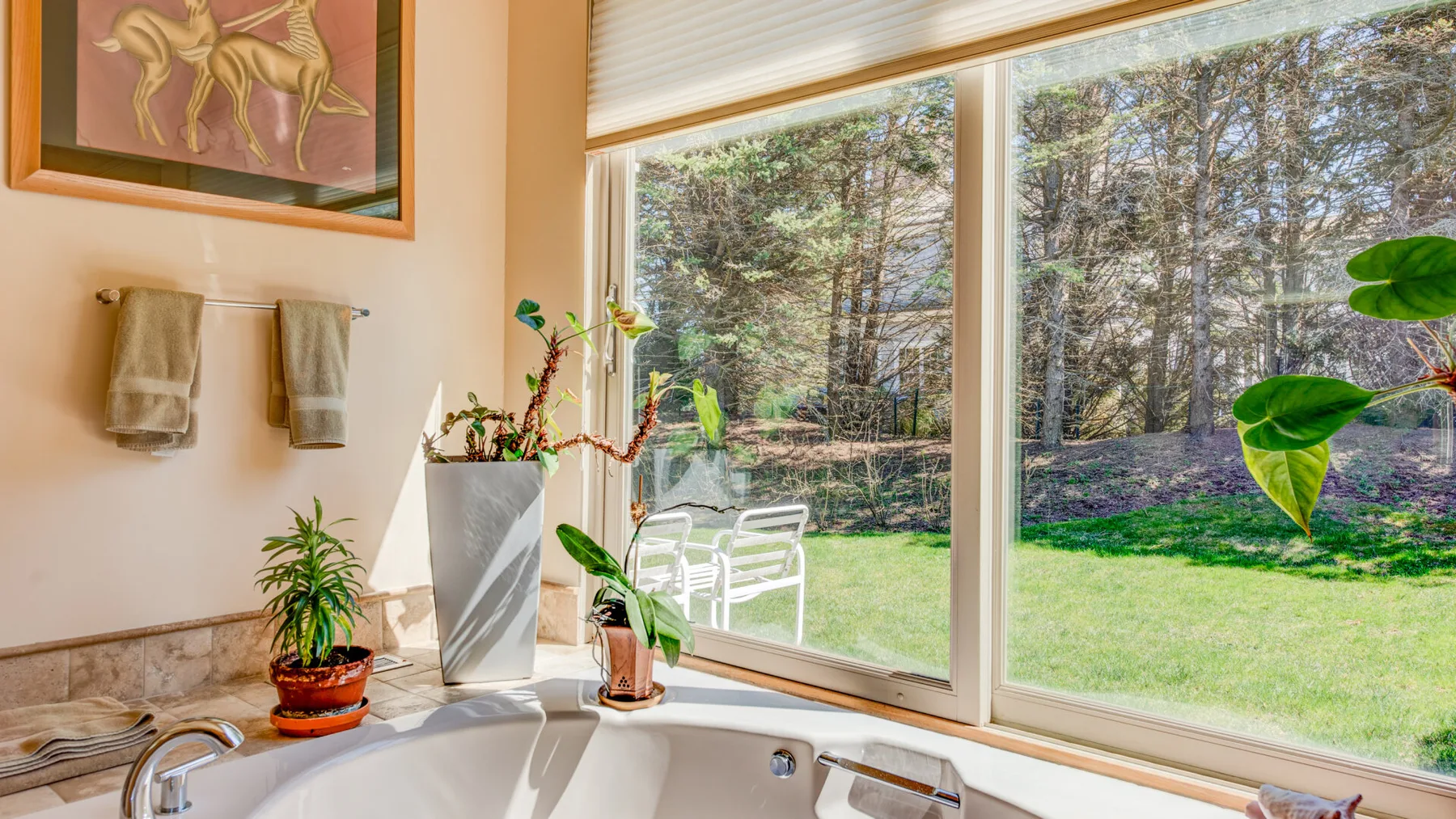 Una habitación luminosa con una bañera junto a grandes ventanas con vistas al jardín.