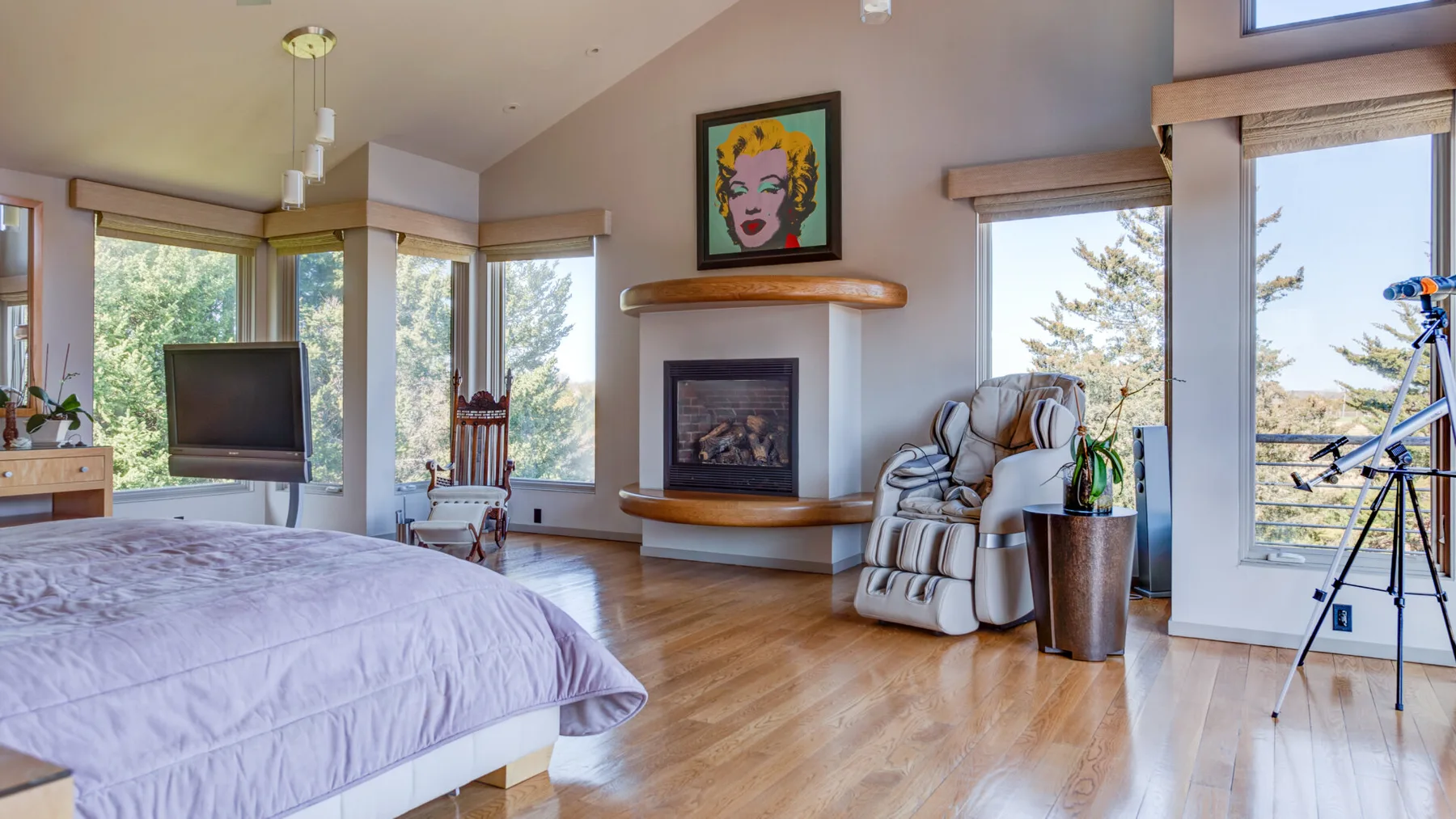 Un dormitorio luminoso con cama, chimenea y ventanales.