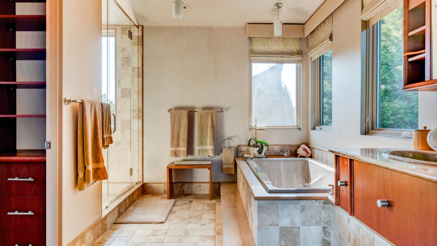 Un baño con bañera, ducha de vidrio y ventanas con vistas a la vegetación.