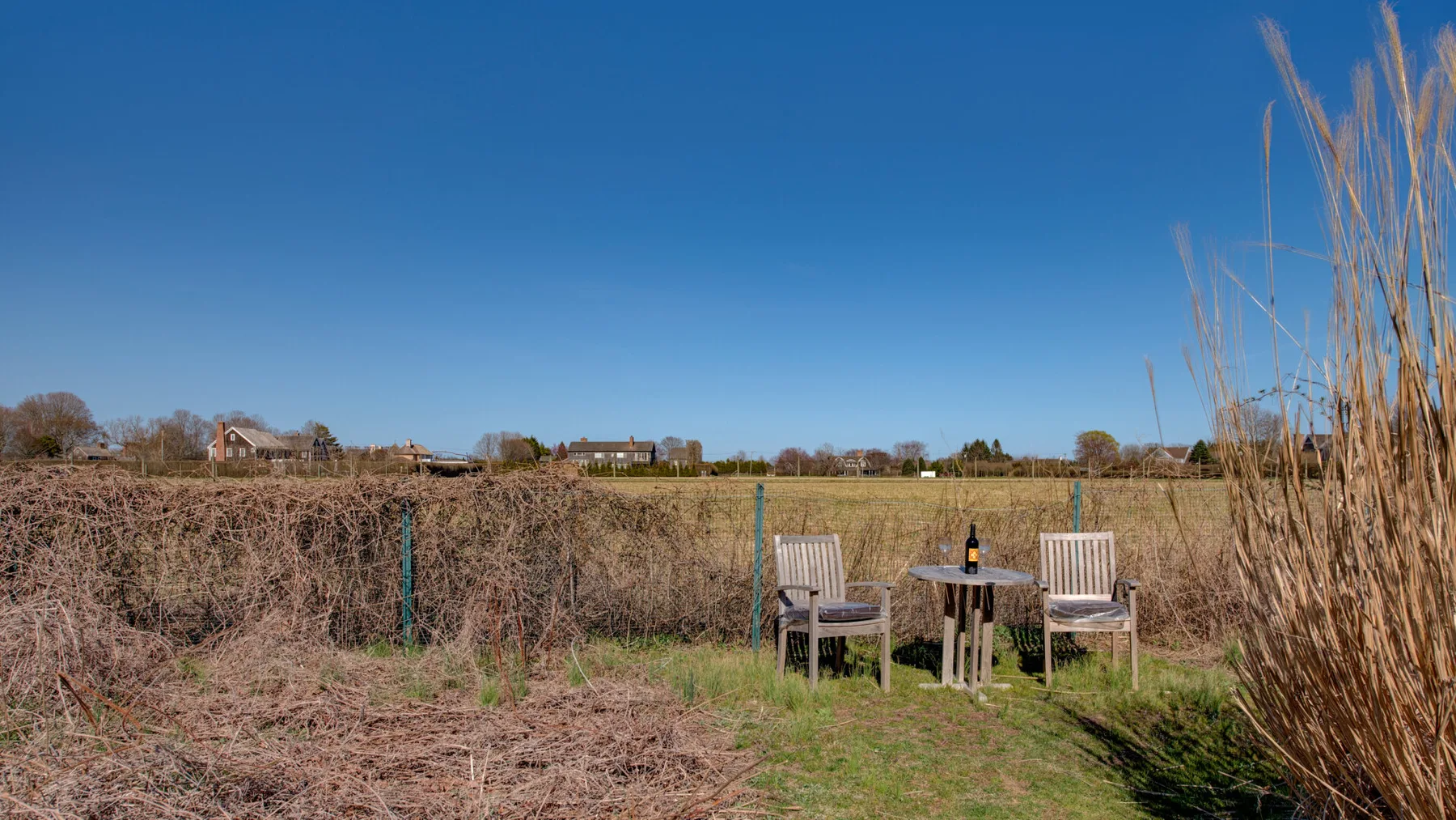Asientos al aire libre junto a un campo, con sillas y una mesa pequeña.