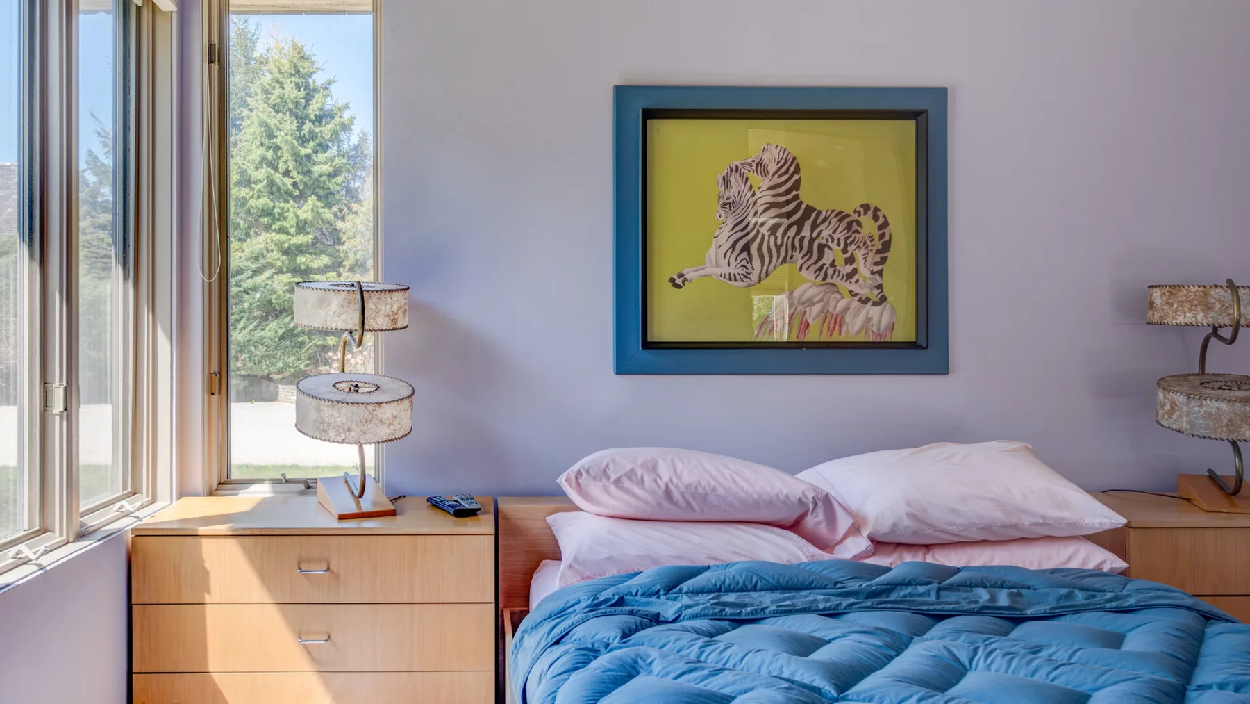 Dormitorio con una cama bajo un cuadro enmarcado de una cebra y junto a una ventana grande.