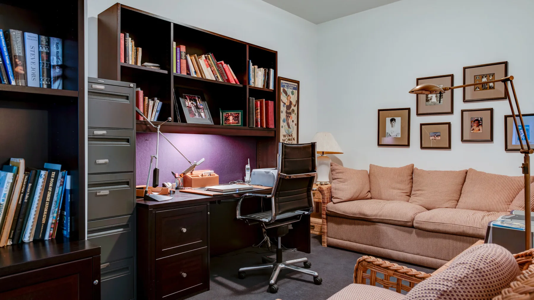 Una sala de estar con un escritorio y estanterías junto a un sofá beige.