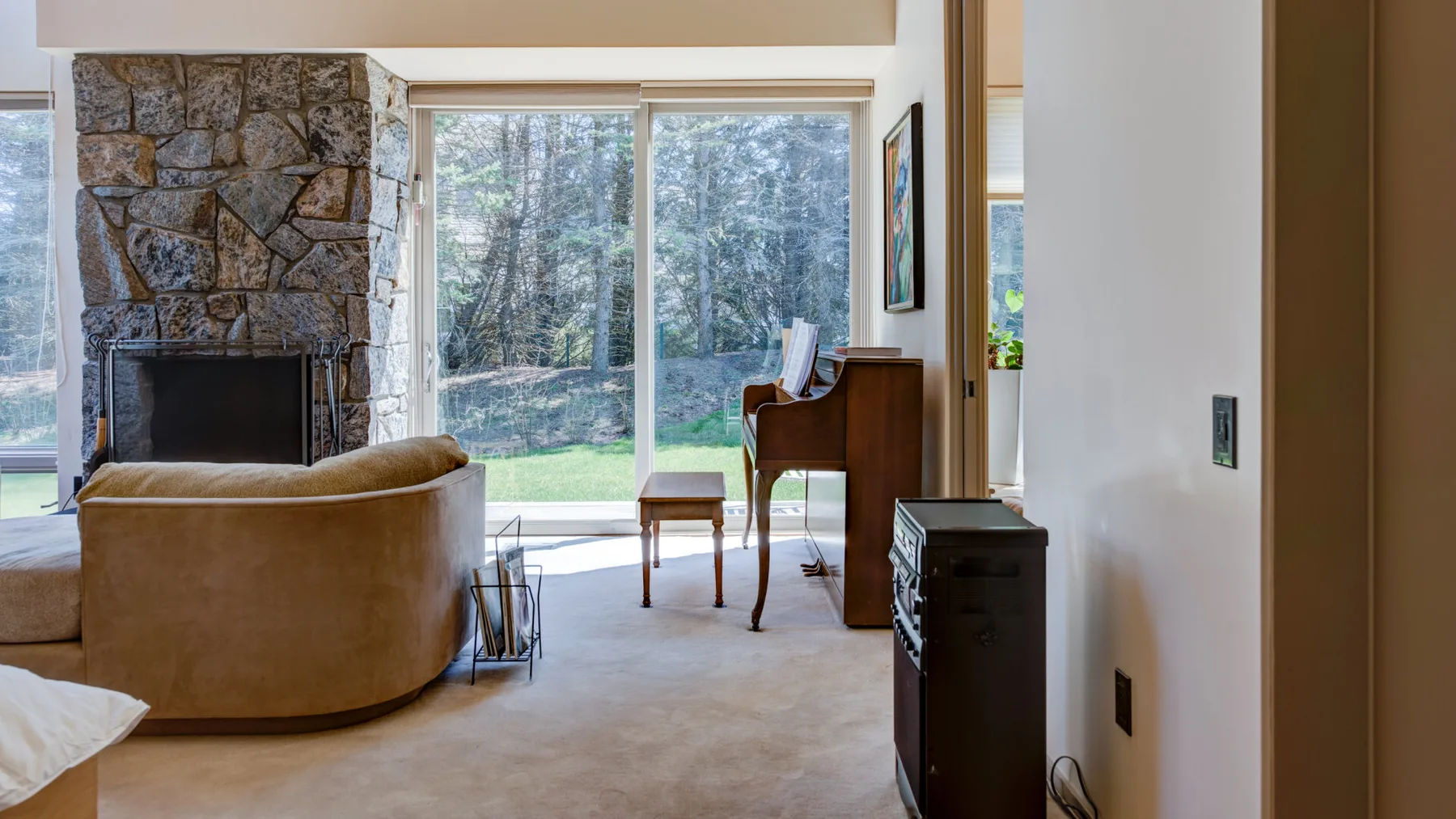 Una sala de estar con asientos, una chimenea de piedra y grandes ventanas frente a los árboles.