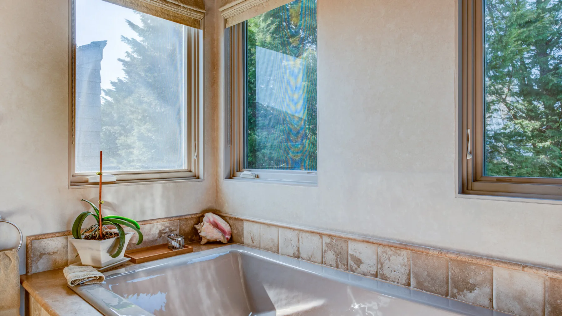 Un baño con una bañera en esquina debajo de varias ventanas.