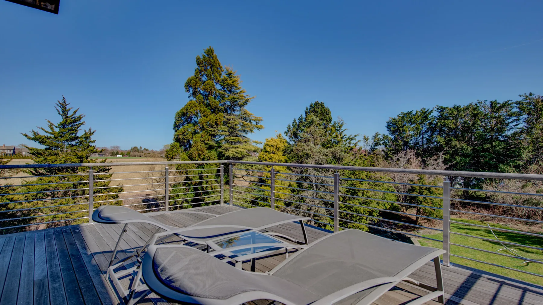 Una terraza soleada al aire libre con asientos reclinables y vistas a los árboles.