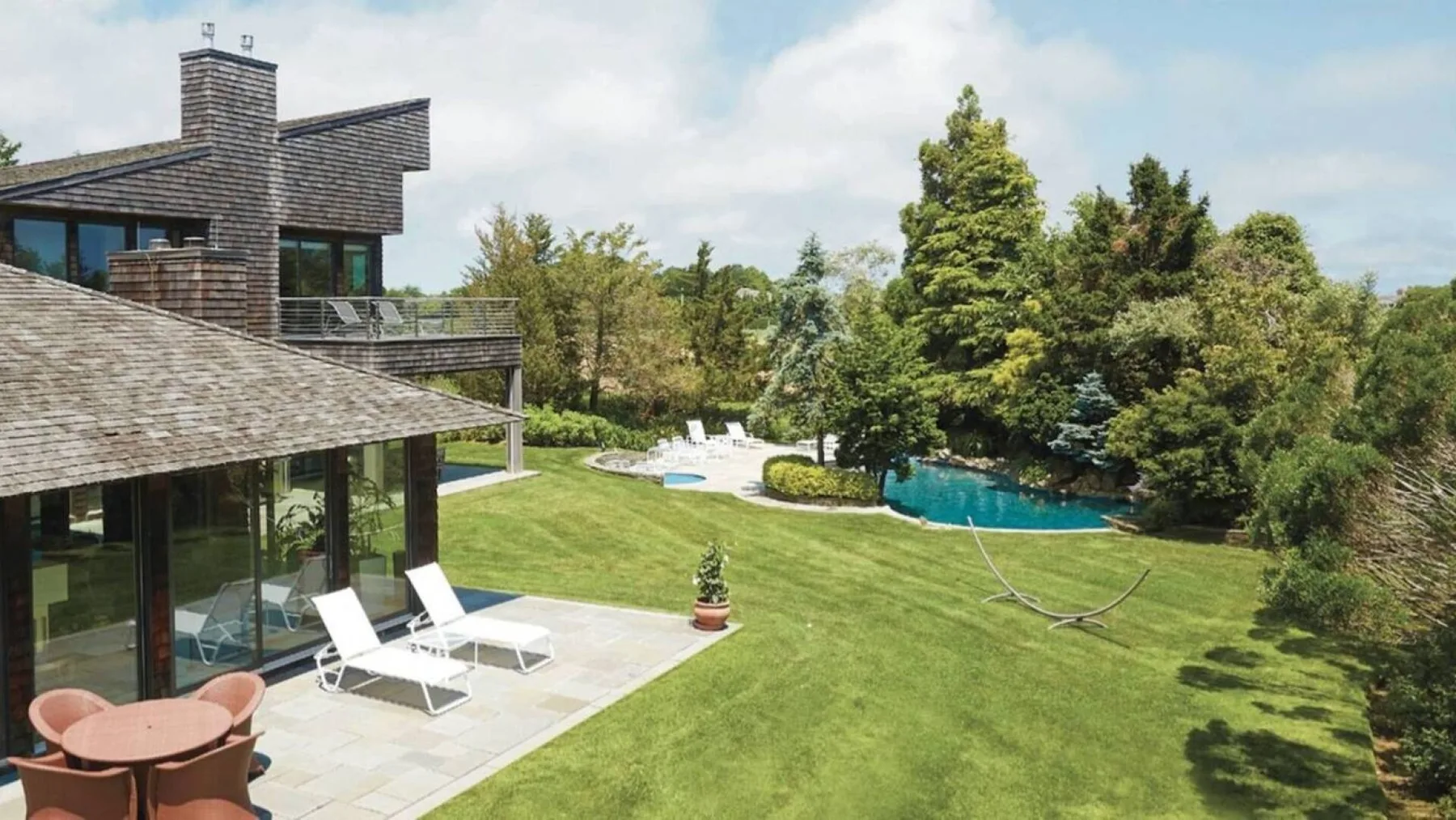 Una casa moderna da a un césped, una terraza con asientos y una piscina.