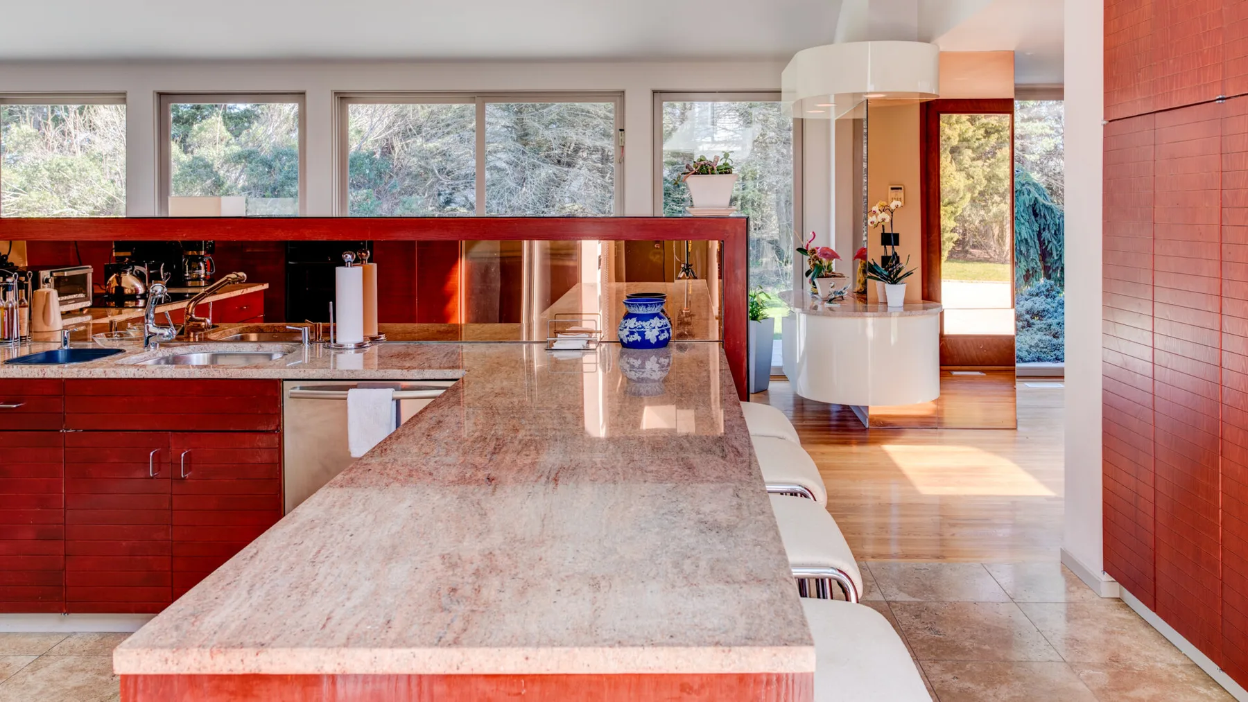 Una cocina moderna con una isla larga de piedra y ventanas con vistas a los árboles.