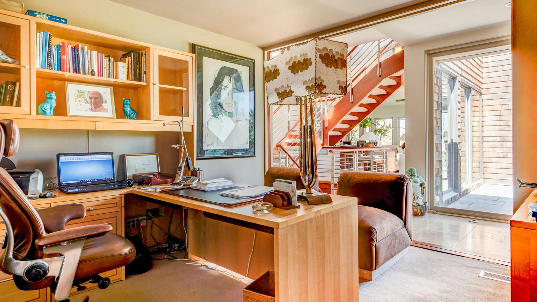 Un despacho en casa con escritorio de madera, estanterías y una escalera al fondo.