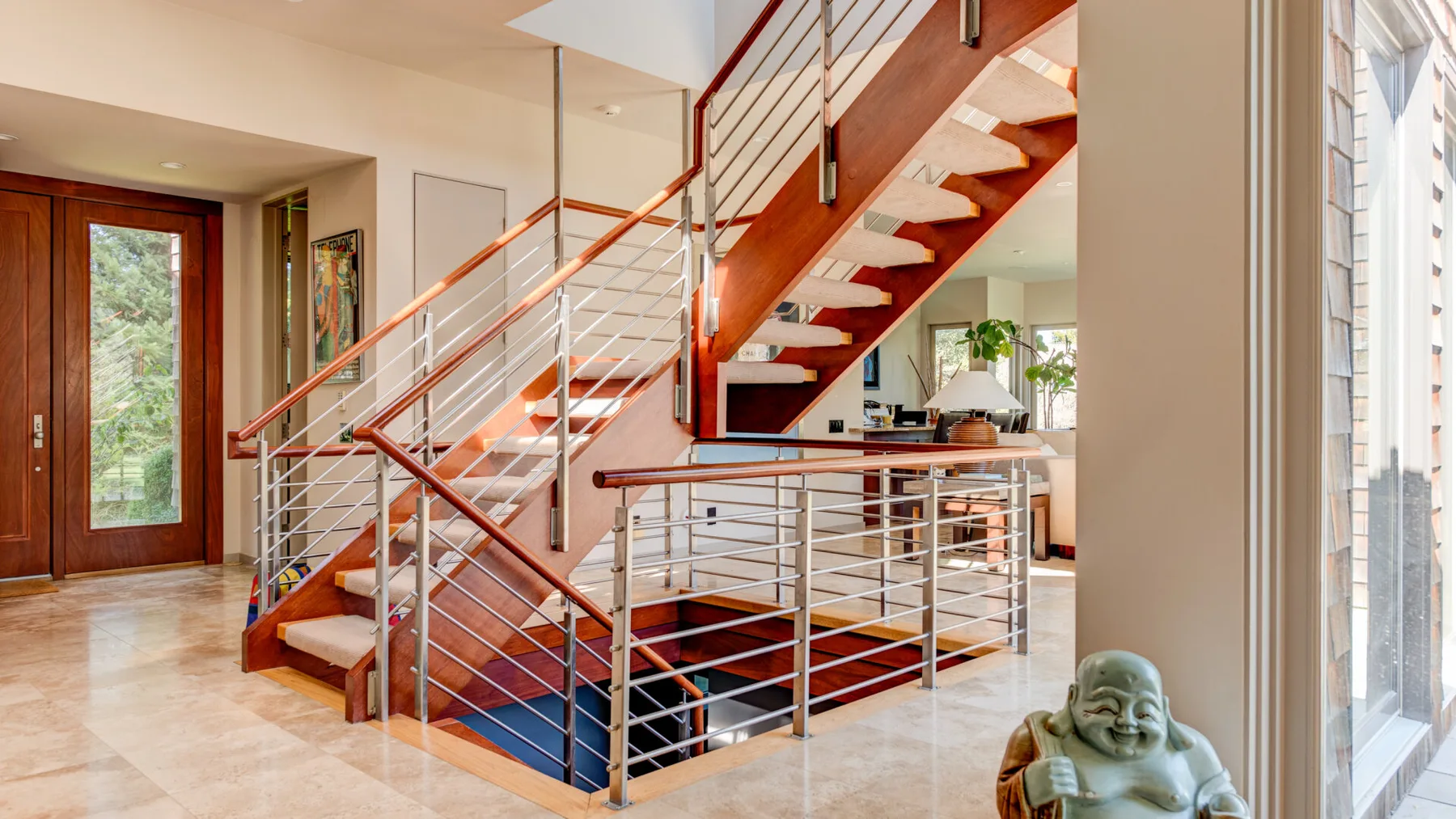 Un interior luminoso muestra una escalera de madera con barandillas metálicas y suelo de baldosas.