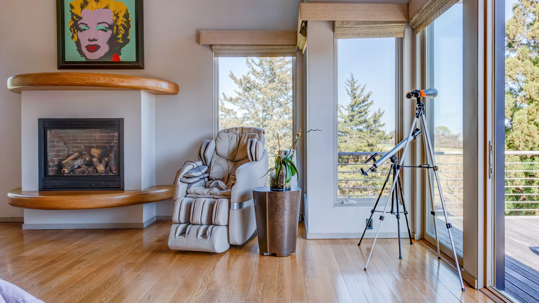 Una sala luminosa tiene una chimenea, asientos reclinables y ventanas grandes.