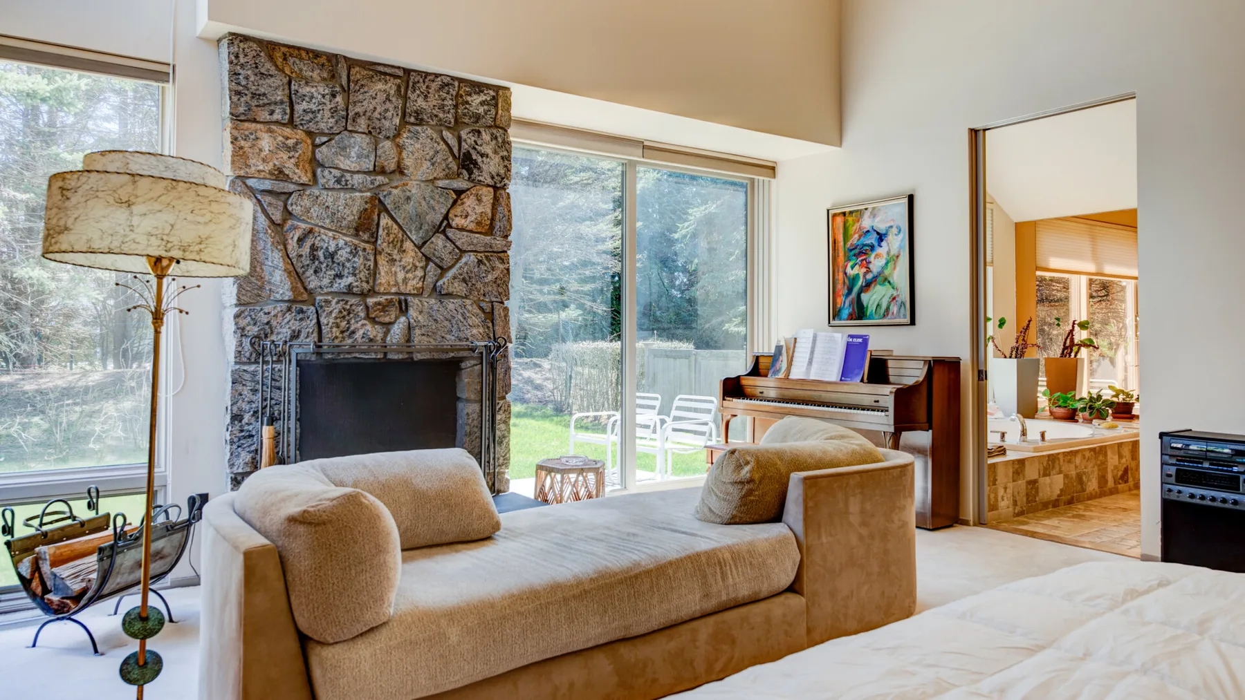 Una sala luminosa con un sofá frente a una chimenea de piedra y grandes ventanas.