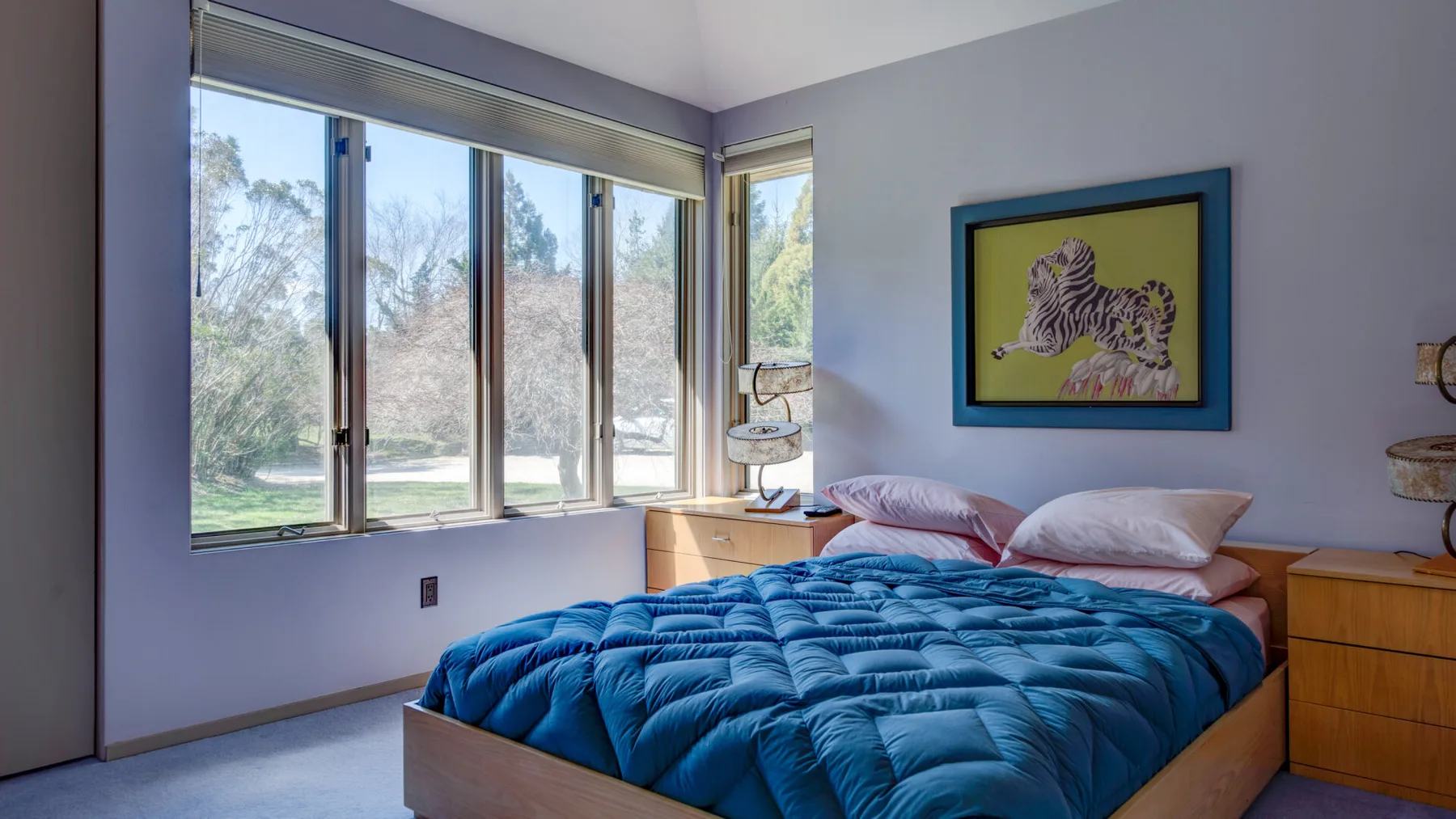Un dormitorio con una cama cubierta con una colcha azul junto a grandes ventanas.