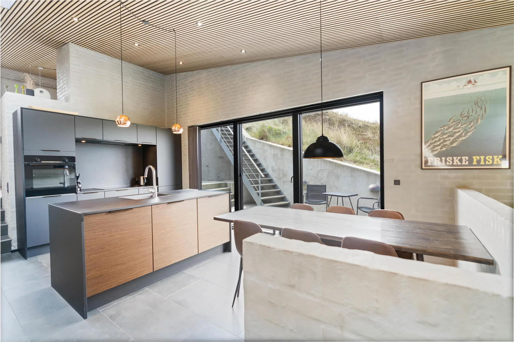 Una cocina moderna y zona de comedor con una mesa larga junto a grandes ventanas.