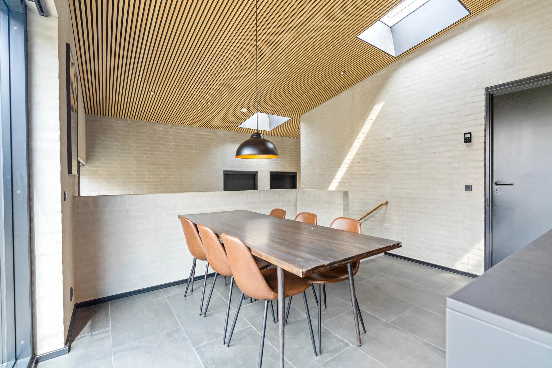 Un comedor con una mesa de madera y sillas bajo una lámpara colgante.