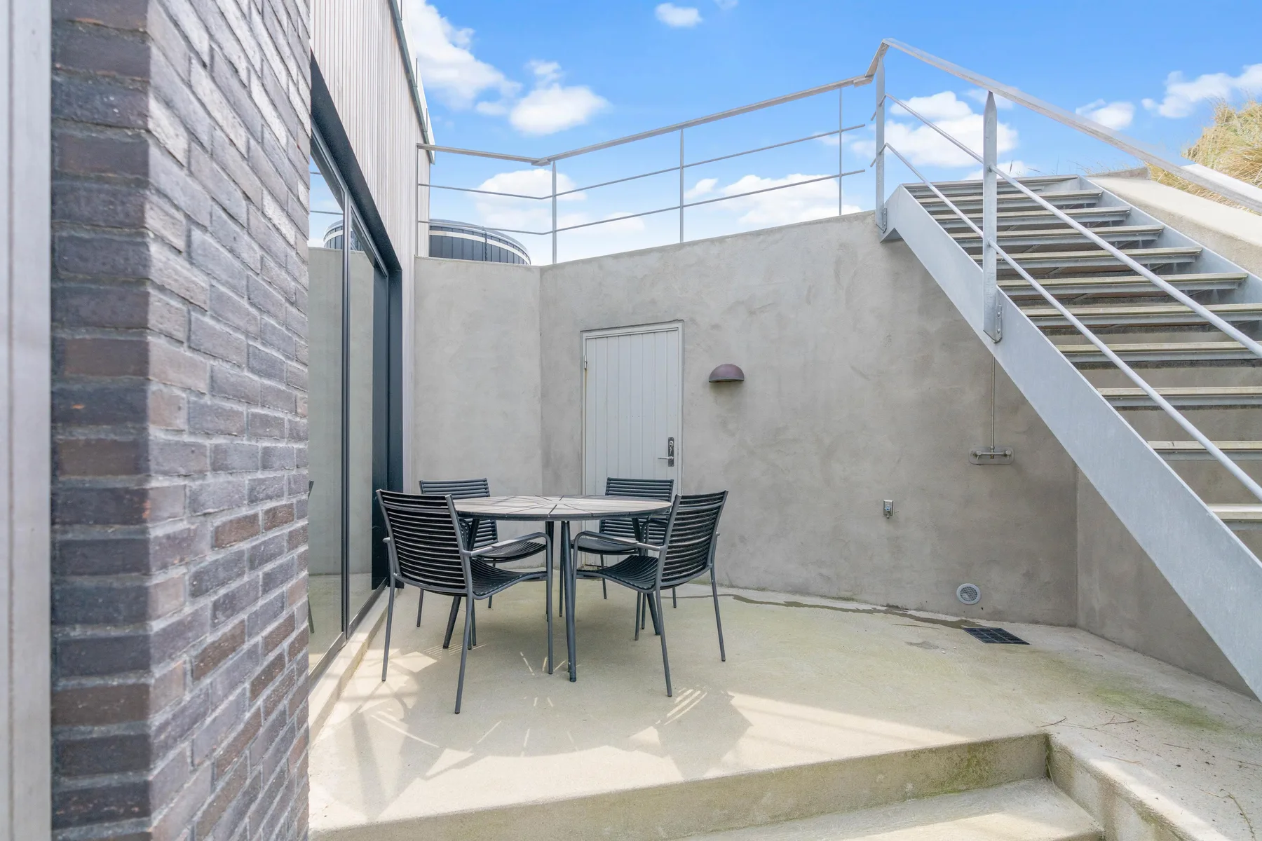 Un patio exterior con una mesa de comedor y asientos junto a una escalera.