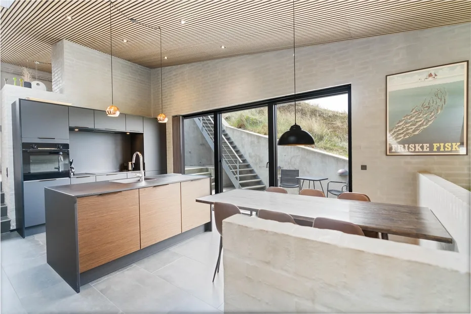 Una cocina moderna y comedor con una mesa larga junto a grandes ventanales.