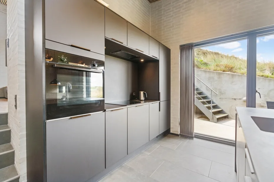 Una cocina moderna con electrodomésticos integrados y una ventana grande que da a unos escalones exteriores.