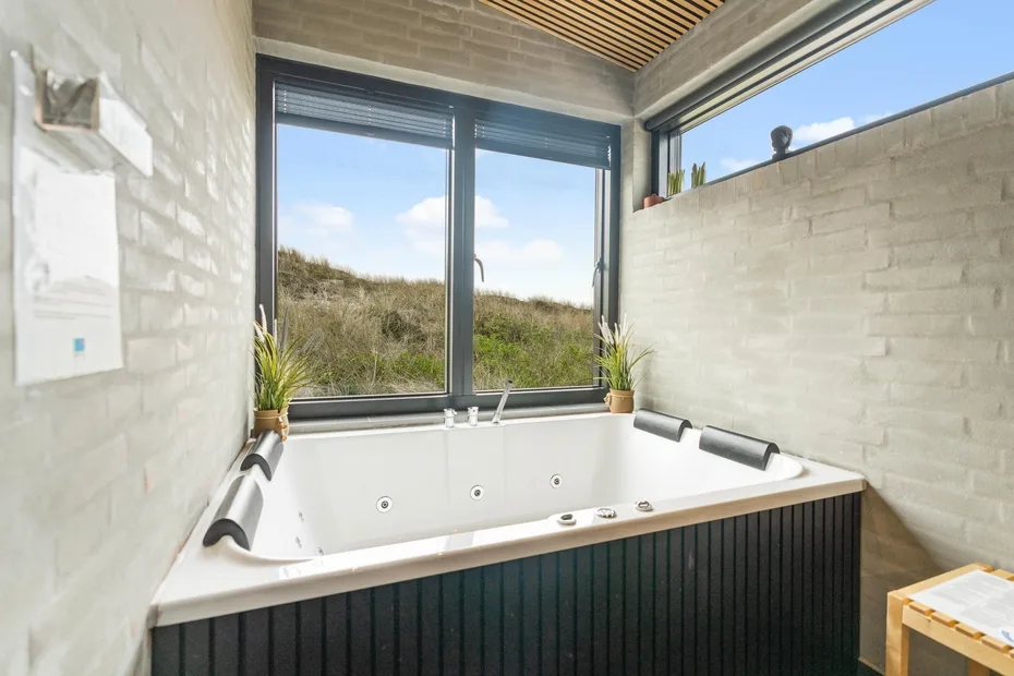 Un baño cuenta con una bañera amplia junto a grandes ventanas con vistas a la vegetación.