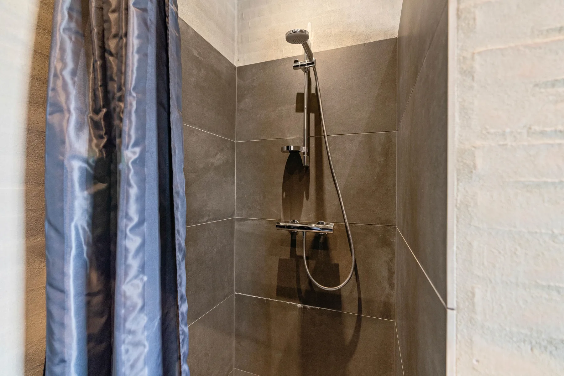 Una ducha con azulejos, ducha de mano y cortina.