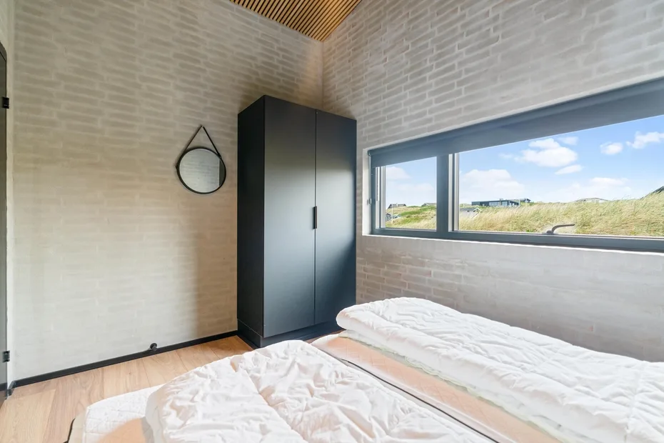 Un dormitorio con un armario oscuro y una ventana amplia con vistas a un terreno cubierto de hierba.