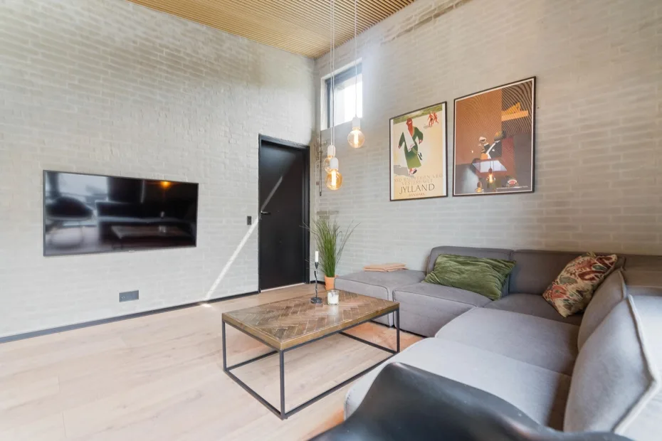 Una sala de estar con asientos seccionales, mesa de centro y televisor en la pared.