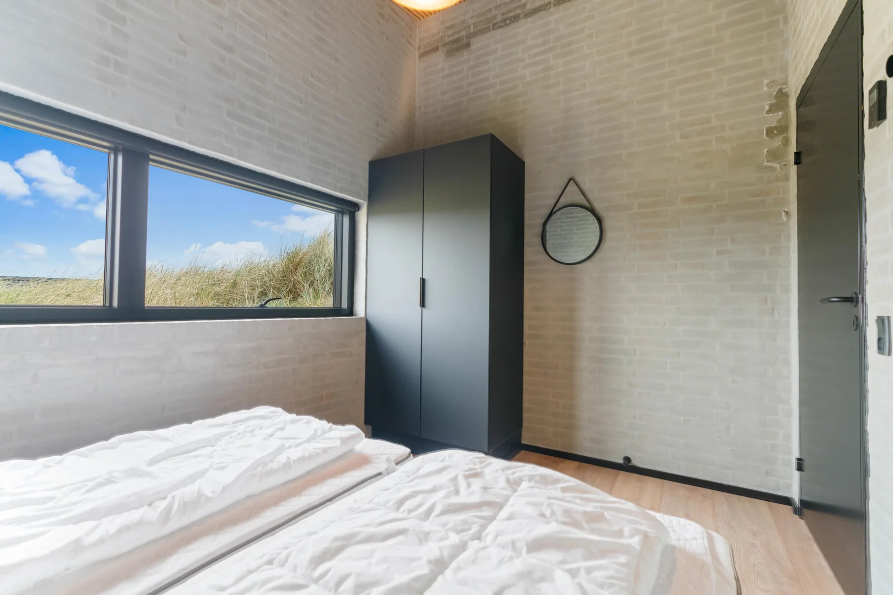 Un dormitorio con una ventana grande, un armario y ropa de cama blanca.