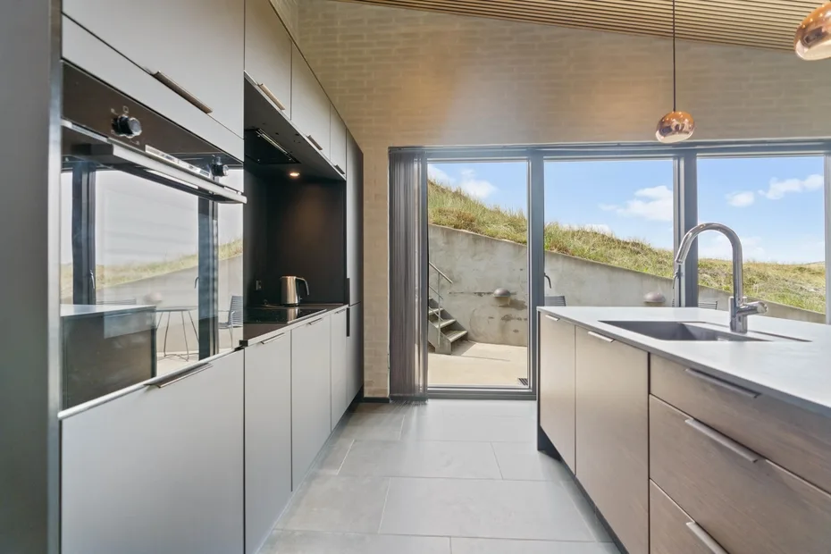 Una cocina moderna con isla central y amplias puertas de vidrio que dan a una vista cubierta de césped.