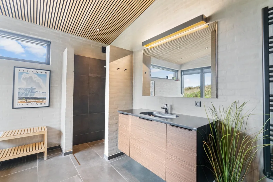 Un baño moderno con un amplio lavabo, espejo de pared y ducha.