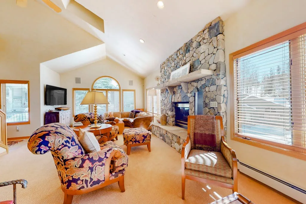 A bright living room with seating arranged around a large stone fireplace.