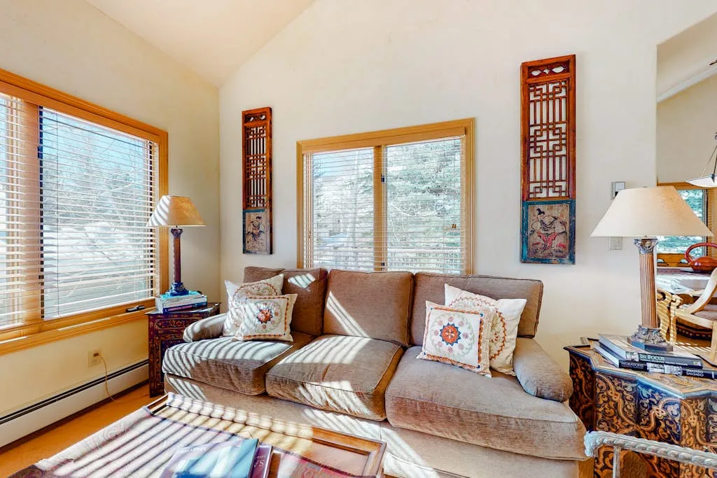 A bright living room with a sofa, patterned cushions, and large windows.