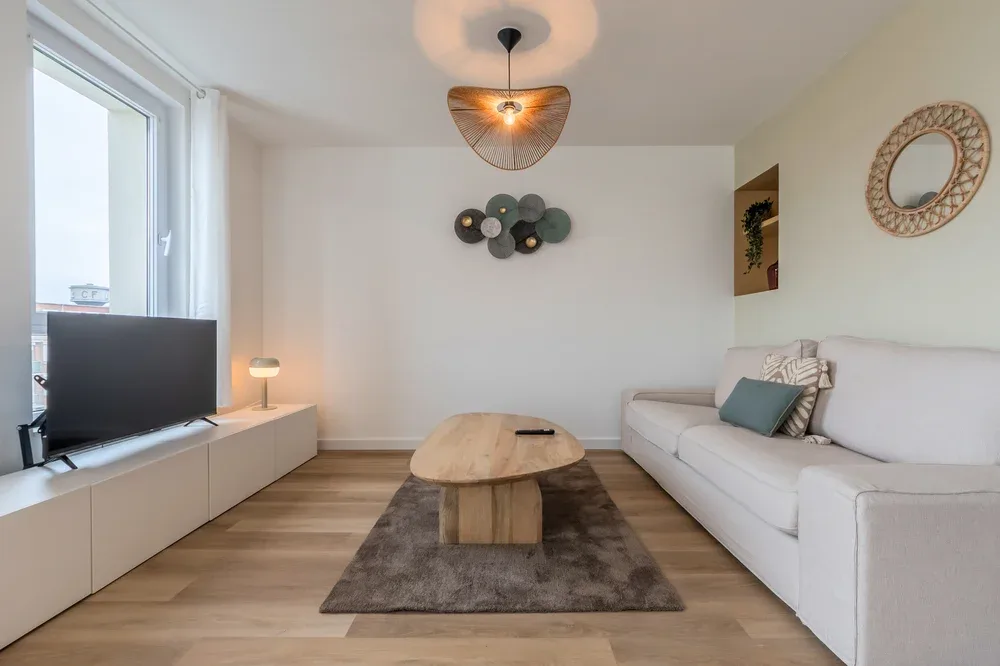 A bright living room with white seating and a television beside the window.