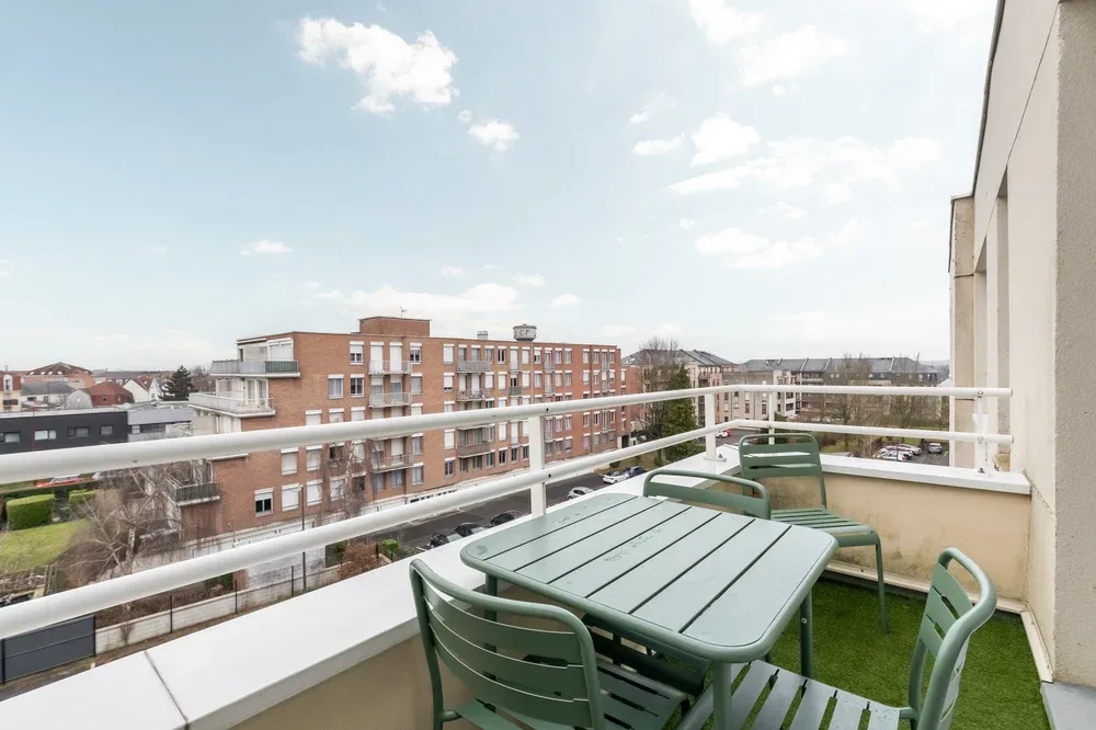 A balcony with outdoor seating overlooks nearby buildings and the surrounding neighborhood.